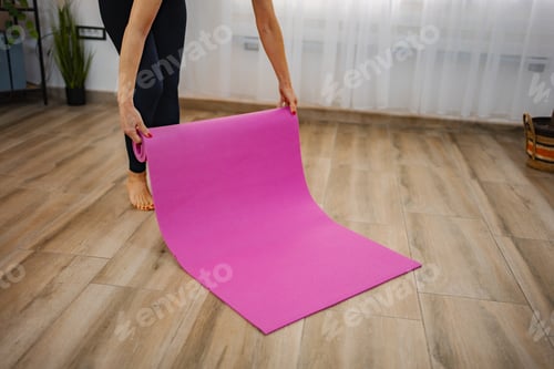 Preview: Woman Rolling Out Exercise Mat on Wooden Floor