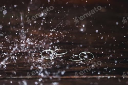 Preview: Double white gold wedding rings under water drops splash close up. Studio macro shot