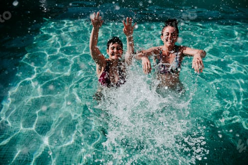Preview: two friends at the pool having fun splashing water. Summer and lifestyle