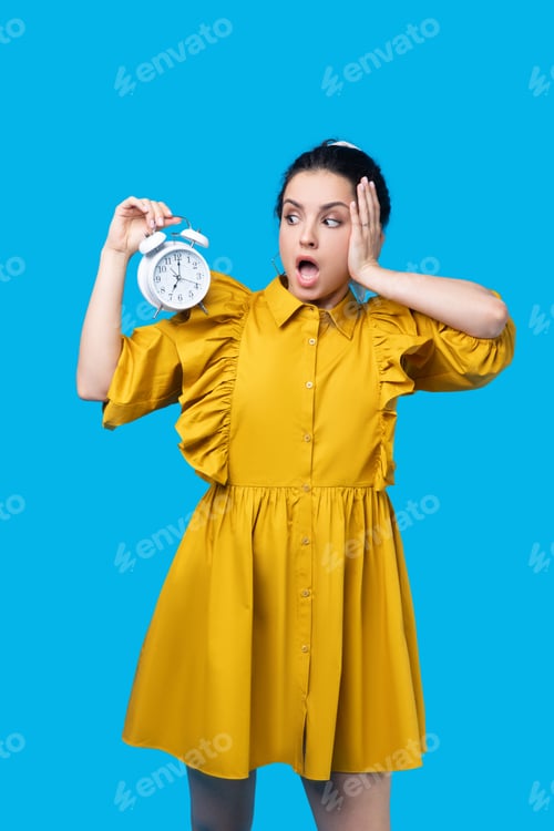 Preview: Woman in a mustard dress holding a clock and looking stressed