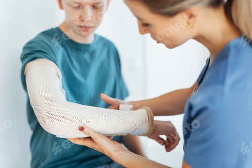 Preview: Doctor checking the orthopedic cast, brace on a teenage patient's broken arm. Teenage boy is healing