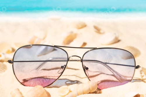 Preview: Purple and pink gradient color sunglasses on beach. Plenty of seashells on tropical sand. Sea view.