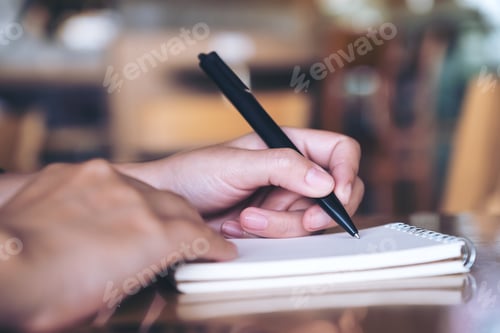Preview: Closeup image of a hand writing down on a white blank notebook on table