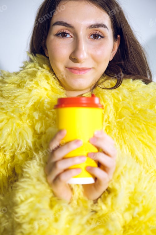 Preview: Attractive girl smiles and holds cup with red lid