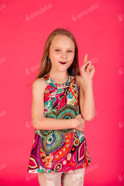 Preview: Portrait of happy little girl in colorful t-shirt index finger up at pink background