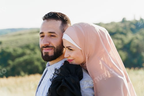 Preview: Muslim couple embraces on green hills, hijab woman glances at her man, dating site ad.