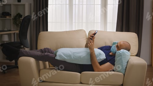 Preview: Bored man with protection mask laying on sofa