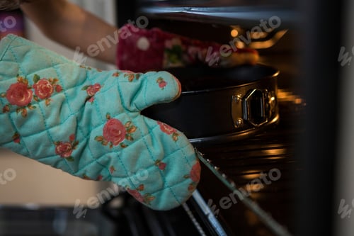 Preview: Cropped hands of girl wearing glove keeping container with cake in oven