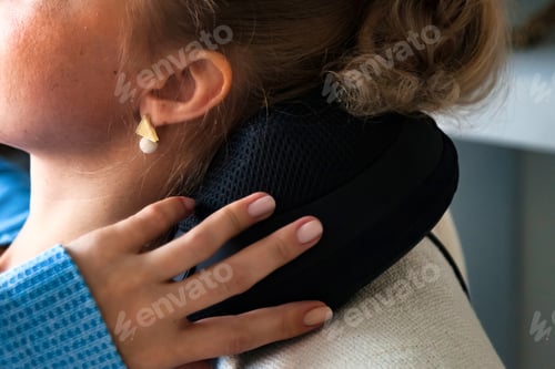 Preview: Woman uses a massage pillow for neck relief and self-care indoors while relaxing at home