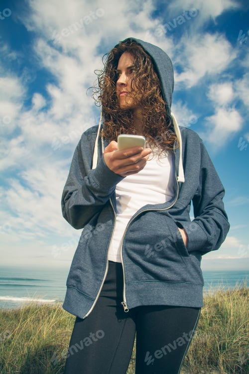 Preview: Young woman with hoodie and sportswear holding smartphone