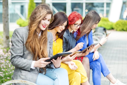 Preview: Four beautiful girls with gadgets are sitting on the bench.