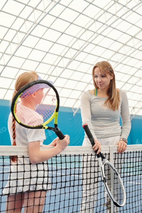 Preview: Young female tennis trainer in activewear and cute girl with tennis rackets