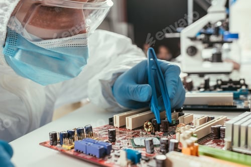 Preview: engineer in medical mask and goggles fixing computer motherboard with tweezers