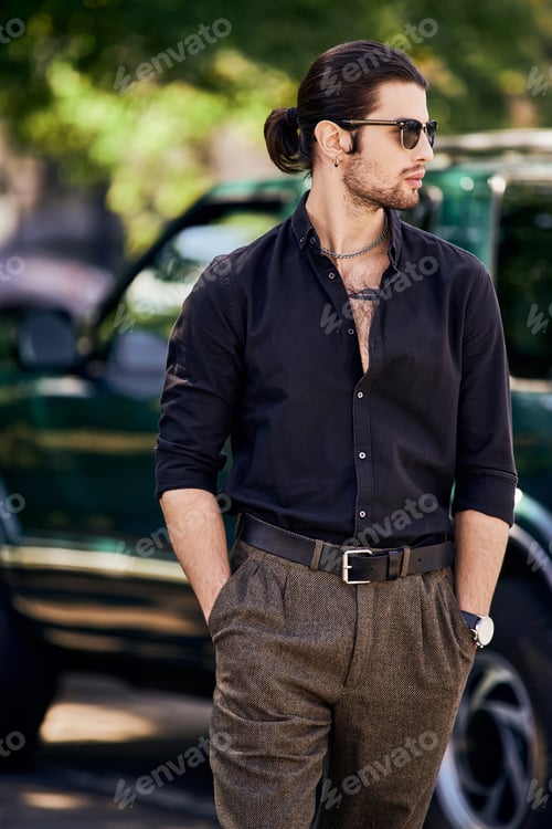 Preview: vertical shot of sexy young man with accessories with hands in pockets posing in front of his car