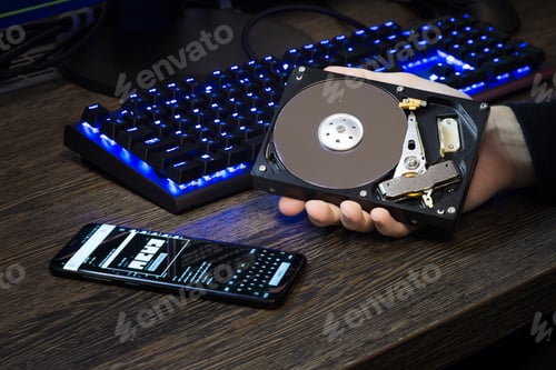Preview: HDD disk in a man's hand against the background of a personal computer and a lying mobile phone next