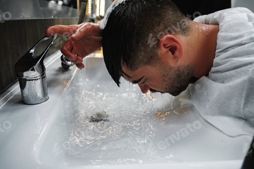 Preview: Hairdresser man washes client head in barbershop, close up