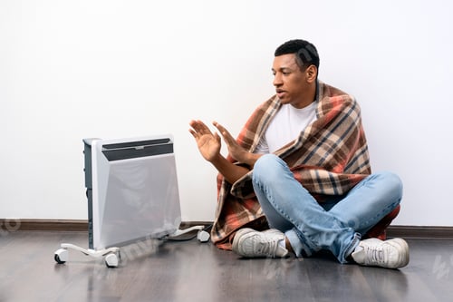 Preview: Frozen man in warm clothes sitting near radiator on a white background