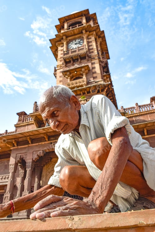 Preview: Indian elderly man with white hair under clock square in brown tones crouching