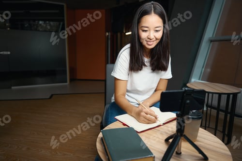 Preview: Charming female taking notes while listening master class on smartphone