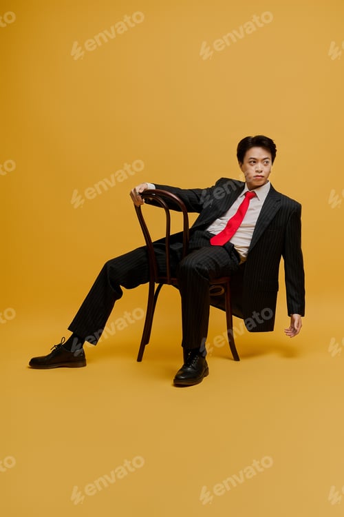 Preview: Confident young Asian businessman in a stylish suit poses in a vibrant studio