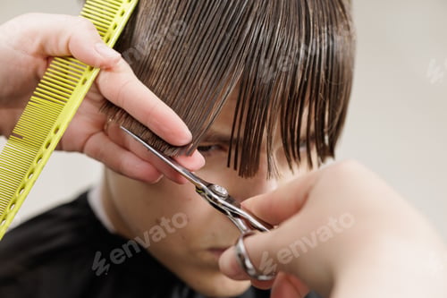 Preview: Hairdresser cutting boy bangs with scissors and comb in barbershop close up