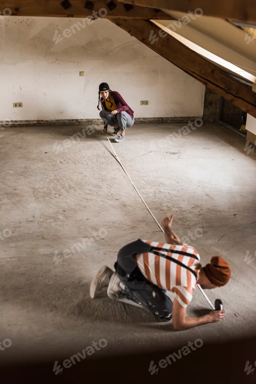 Preview: Young man and woman measuring floor on construction site