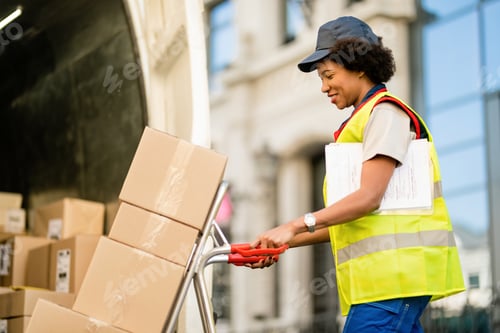 Preview: Happy African American deliverer with hand truck unloading packages from a van.