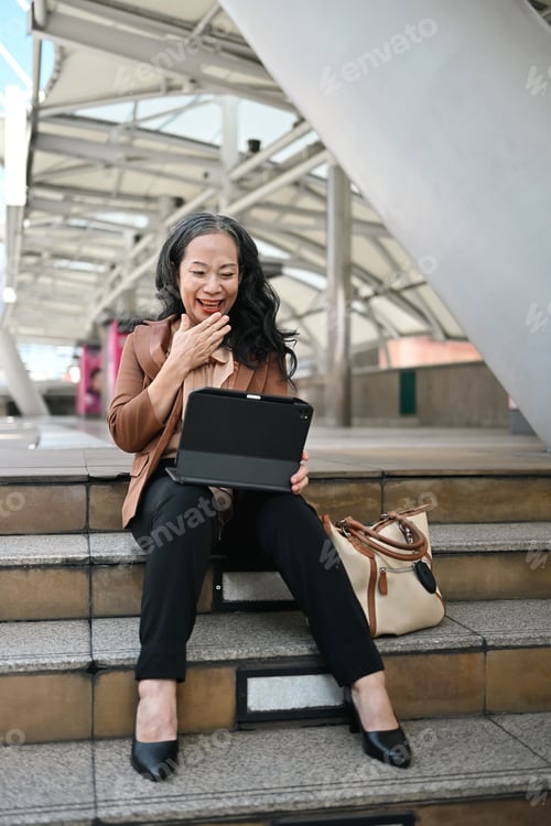 Vista previa: Alegre empresaria senior que usa una tableta digital en los escalones del centro