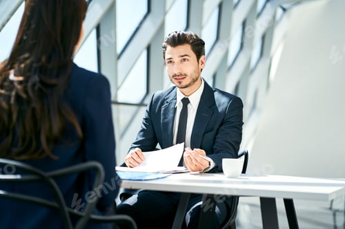 Preview: Businessman looking at businesswoman in modern office