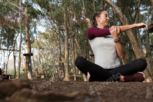 Preview: Woman stretching right arm across chest in forest rope course wearing watch, sneakers, copy space