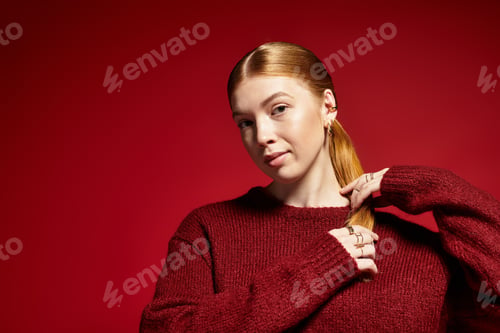 Preview: Young woman with red hair showcases winter fashion on bold red background