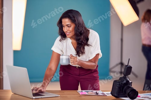 Preview: Mature Female Photographer Checking Images On Laptop During Shoot In Studio