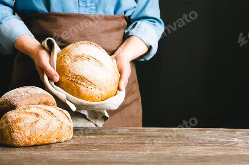 Preview: Woman holds in her hands loaf of freshly bread rustic background. home-made diet baking without