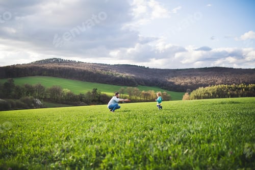 Preview: A father with his toddler son running outside in spring nature.