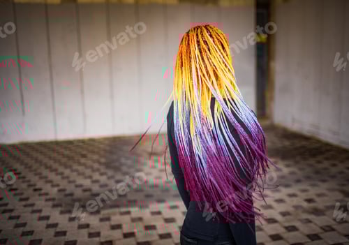 Preview: Standing back to camera, a fashionable girl in a jacket straightens her colored african braids