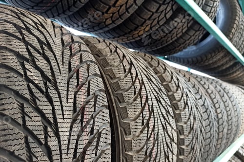 Preview: Many black rubber car tires on store shelf for sale.