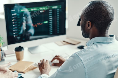 Preview: Rear view of young African man in shirt using computer while working in the office