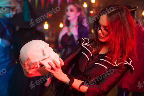 Preview: Halloween witch with a skull in front of her monster friends at halloween party