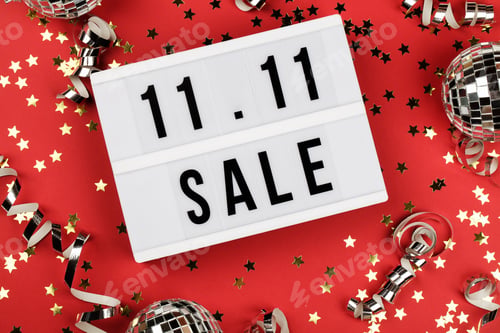 Preview: 11.11 sale text on white lightbox, holiday ribbon, small stars and disco balls on red background.