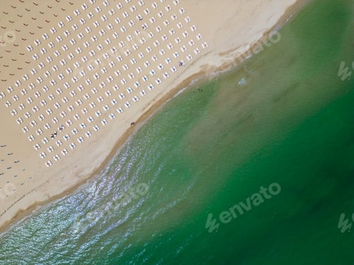 Preview: A sandy beach stretches along the seaside, adorned with empty sun loungers. Aerial view