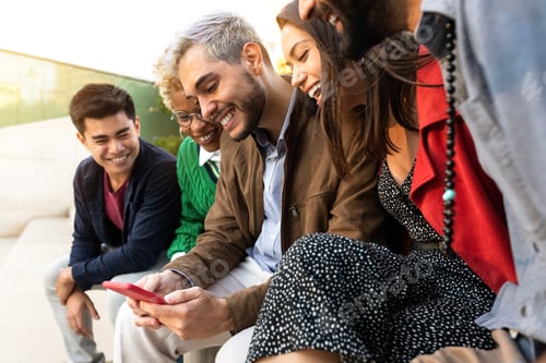 Preview: Multiracial friends sit on a bench looking at cellphone together. Watching online video.