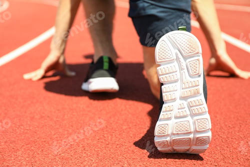 Preview: Sportsman low starting to run on red athletic track, close up
