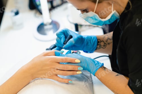 Preview: Close-up of Beautician painting her client's nails in blue and yellow nail varnish