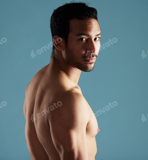 Preview: Handsome young hispanic man standing shirtless in studio isolated against a blue background. Mixed