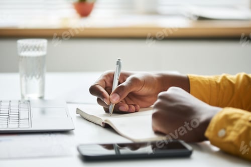 Preview: Focus on hand of young businessman holding pen over page of open notepad