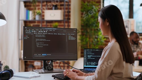Preview: Asian woman is seen typing code for an app development project on her computer