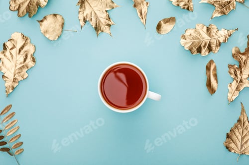Preview: top view of warm tea in mug near golden foliage on blue background