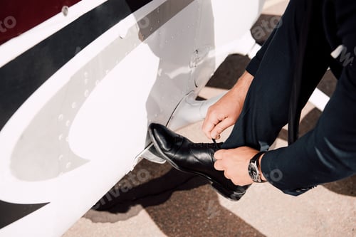 Preview: cropped view of businessman in formal wear tying shoelaces near plane