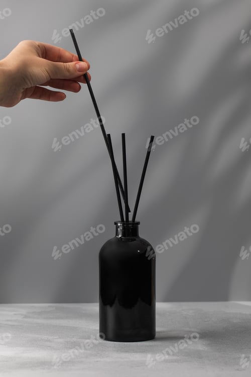 Preview: A woman puts a bamboo stick in a glass bottle with perfume for the house. Interior perfume