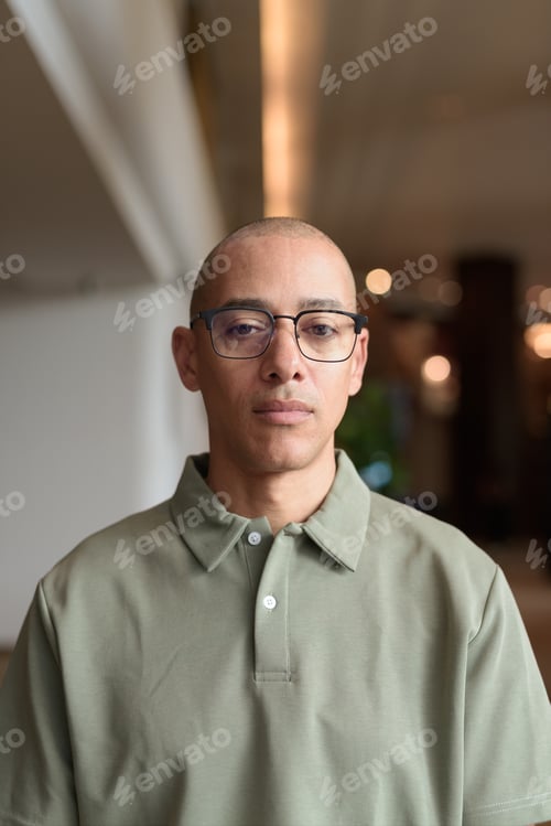 Preview: Bald Hispanic man face in hotel lobby with eyeglasses, stylish confident portrait in casual setting